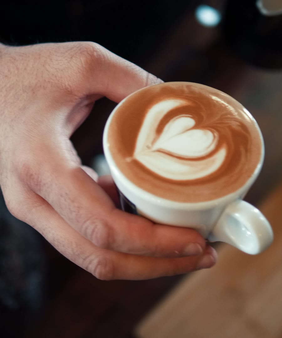 A hand holding a latte with a heart poured in the foam